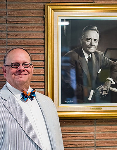 库泽创造了音乐的传统,关怀 4 Photo of Robin Koozer standing next to a framed portrait of Hayes M. Fuhr.